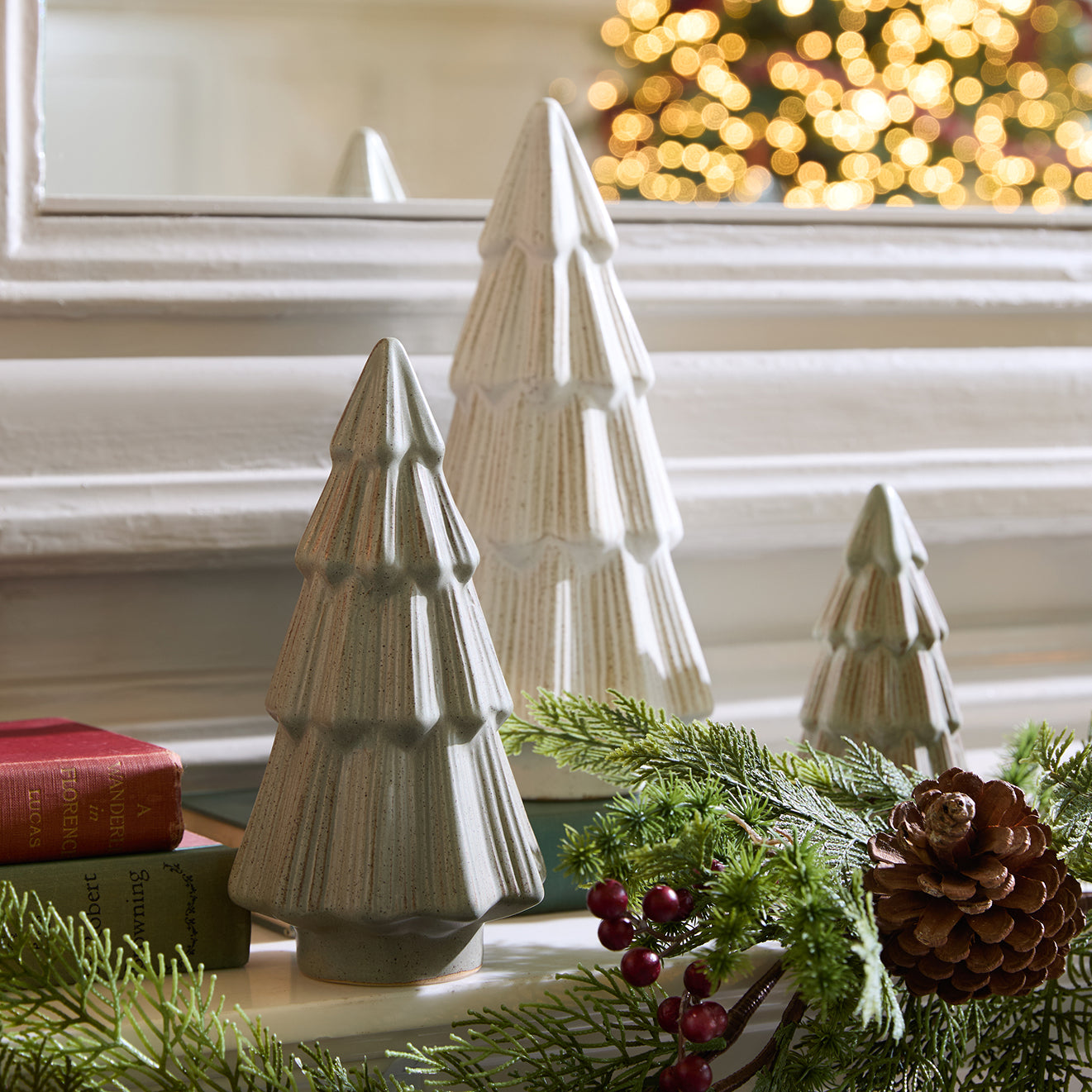 Decorative Christmas trees on a table with greenery and a blurred festive background