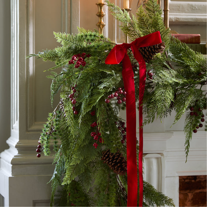 Decorative Christmas garland with red ribbon and pinecones against a neutral wall.