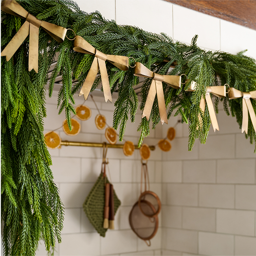 Decorative greenery with ribbons and hanging kitchen utensils against a tiled wall.