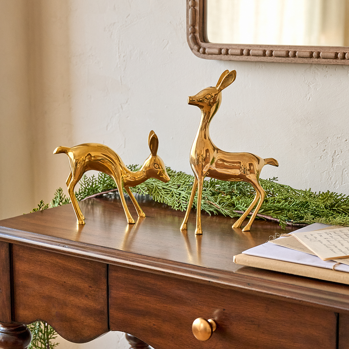 Two gold deer figurines on a wooden surface with a mirror in the background.