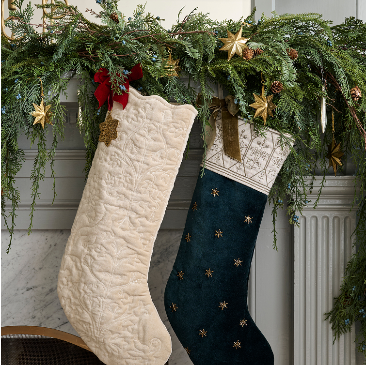 Two Christmas stockings hanging on a decorated fireplace mantel with greenery and stars.