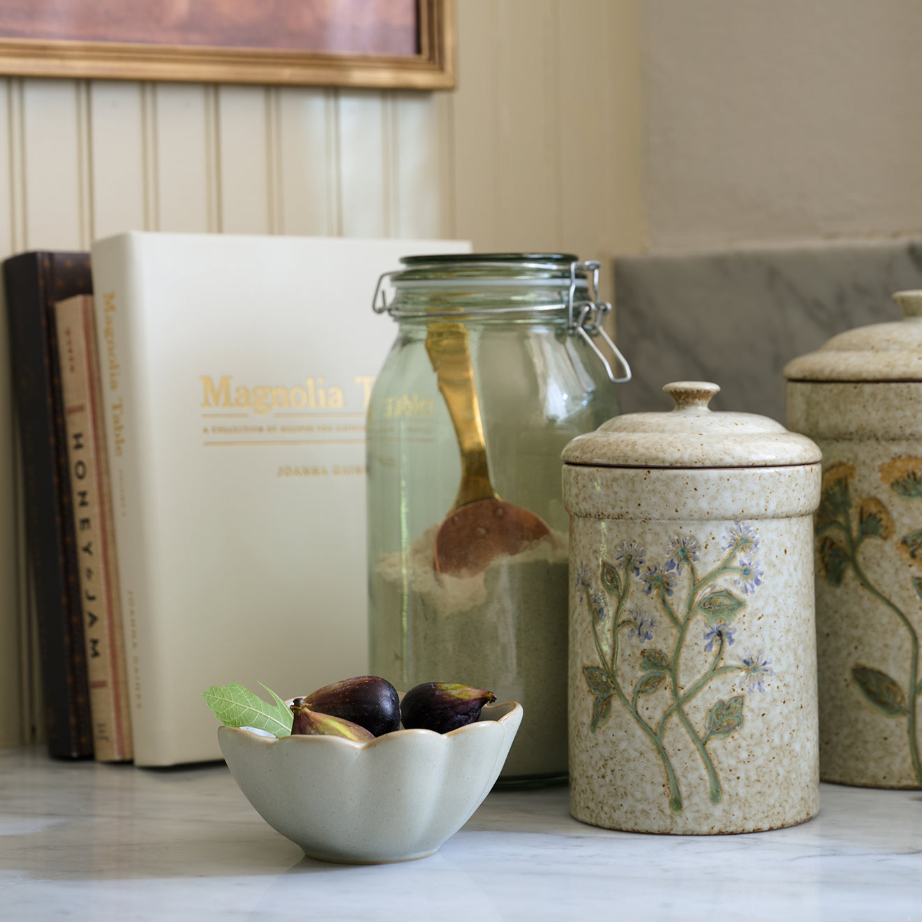 Decorative items including a glass jar, ceramic canisters, and a small bowl with figs on a surface.