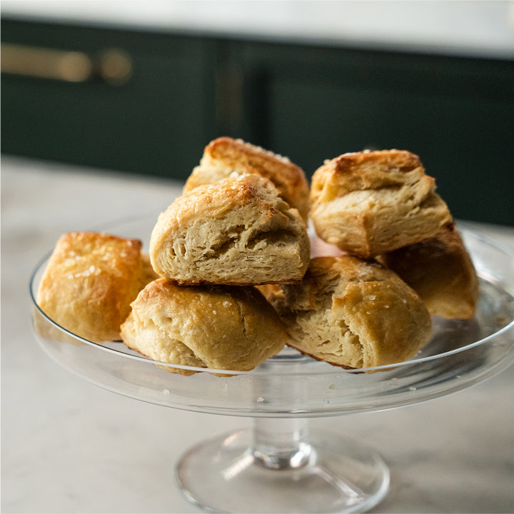 Biscuits stacked on a glass cake stand with a blurred kitchen background