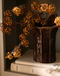 Brown vase with dried flowers on a shelf with books