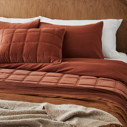 Brown quilted bedding set on a bed with white pillows against a wooden headboard.  Shop red and pink bedding.