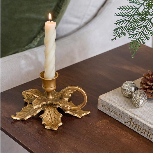 Decorative gold candle holder with a lit candle on a wooden surface.