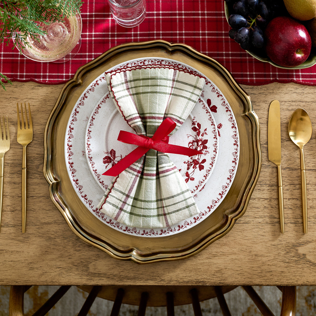 Dining table setting with a decorative plate, gold charger, and red ribbon.