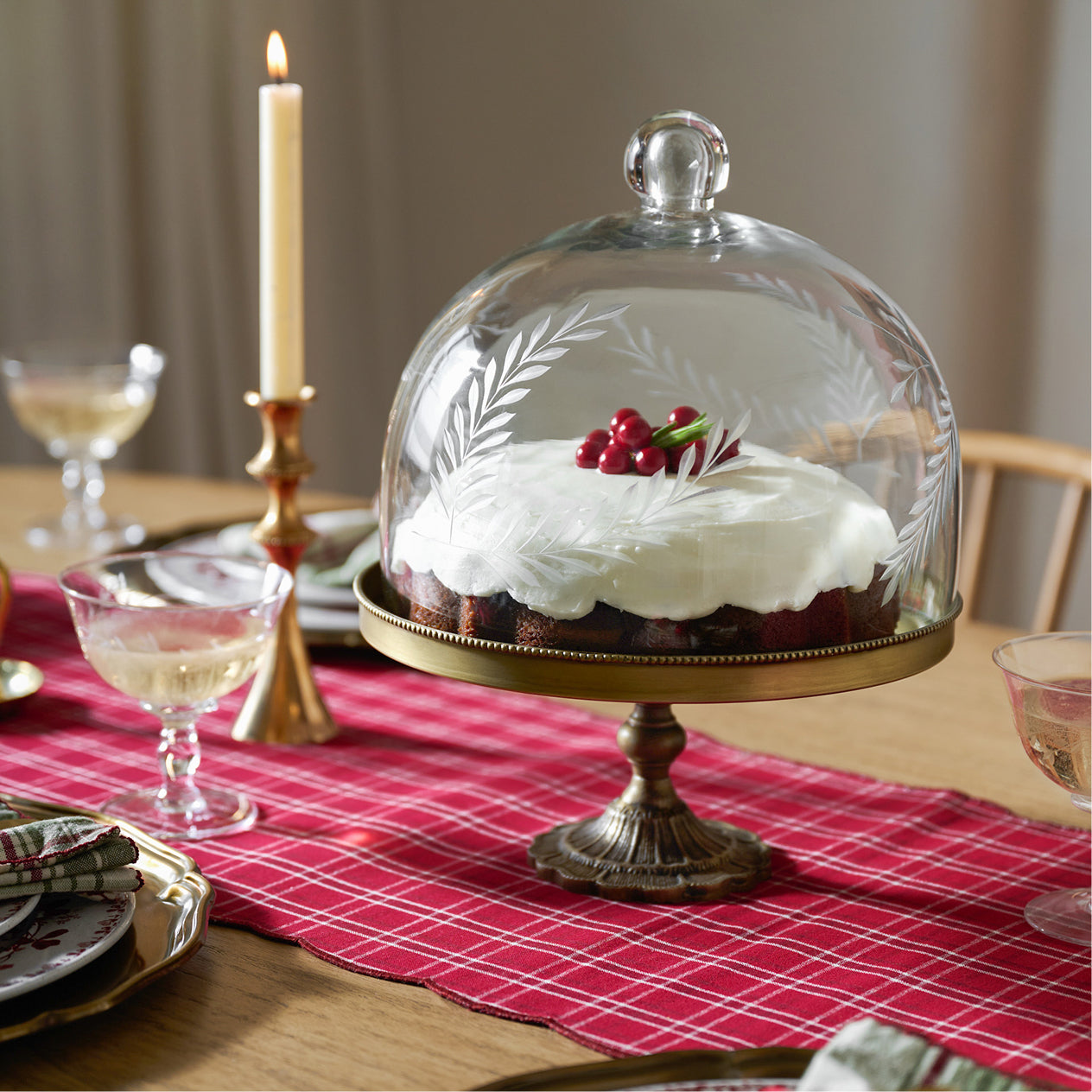Decorative cake under a glass dome on a table with a red checkered tablecloth.