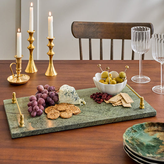 Dining table with a marble platter of cheese, crackers, and fruit, accompanied by candles and wine glasses.