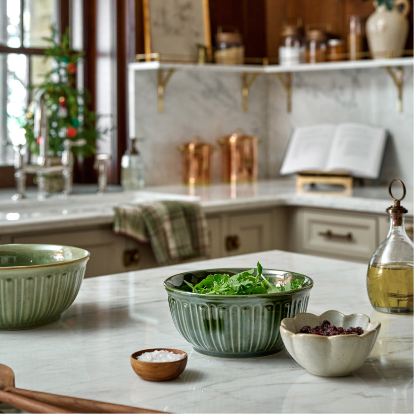Kitchen counter with green bowls containing salad and ingredients, with a blurred background of a kitchen.