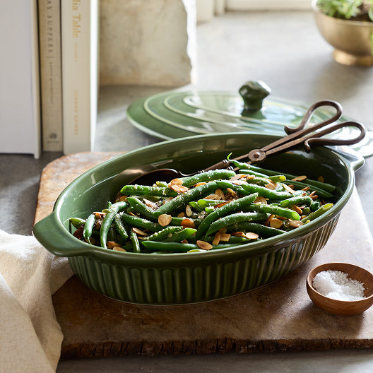 Green bean casserole in a green ceramic dish on a wooden cutting board.