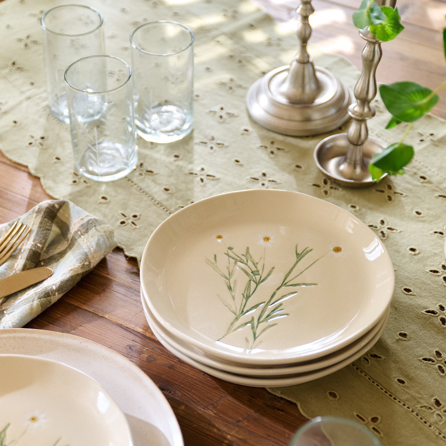 Set of ceramic plates with floral design on a table with glasses and cutlery.