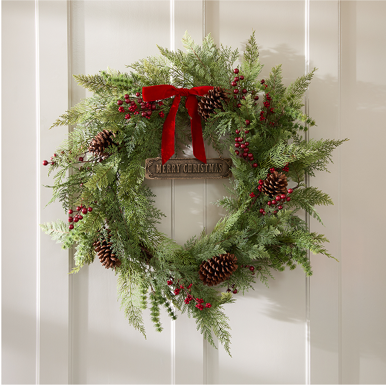 Christmas wreath with greenery, red berries, pinecones, and a red ribbon on a white door.
