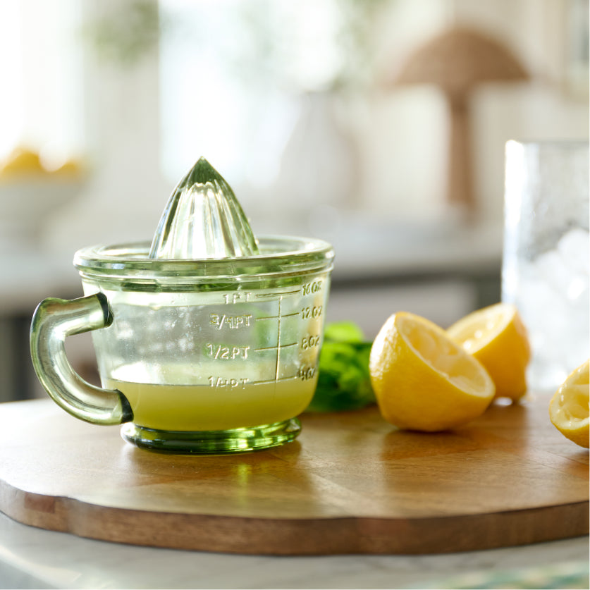 Green glass citrus juicer with green handle on a wooden surface with lemons.