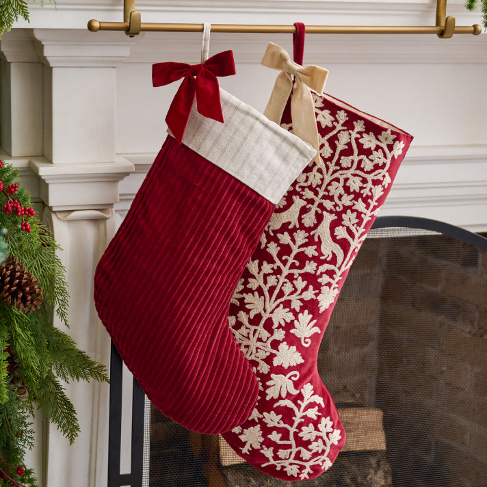 Two Christmas stockings hanging on a fireplace mantle with decorative ribbons.