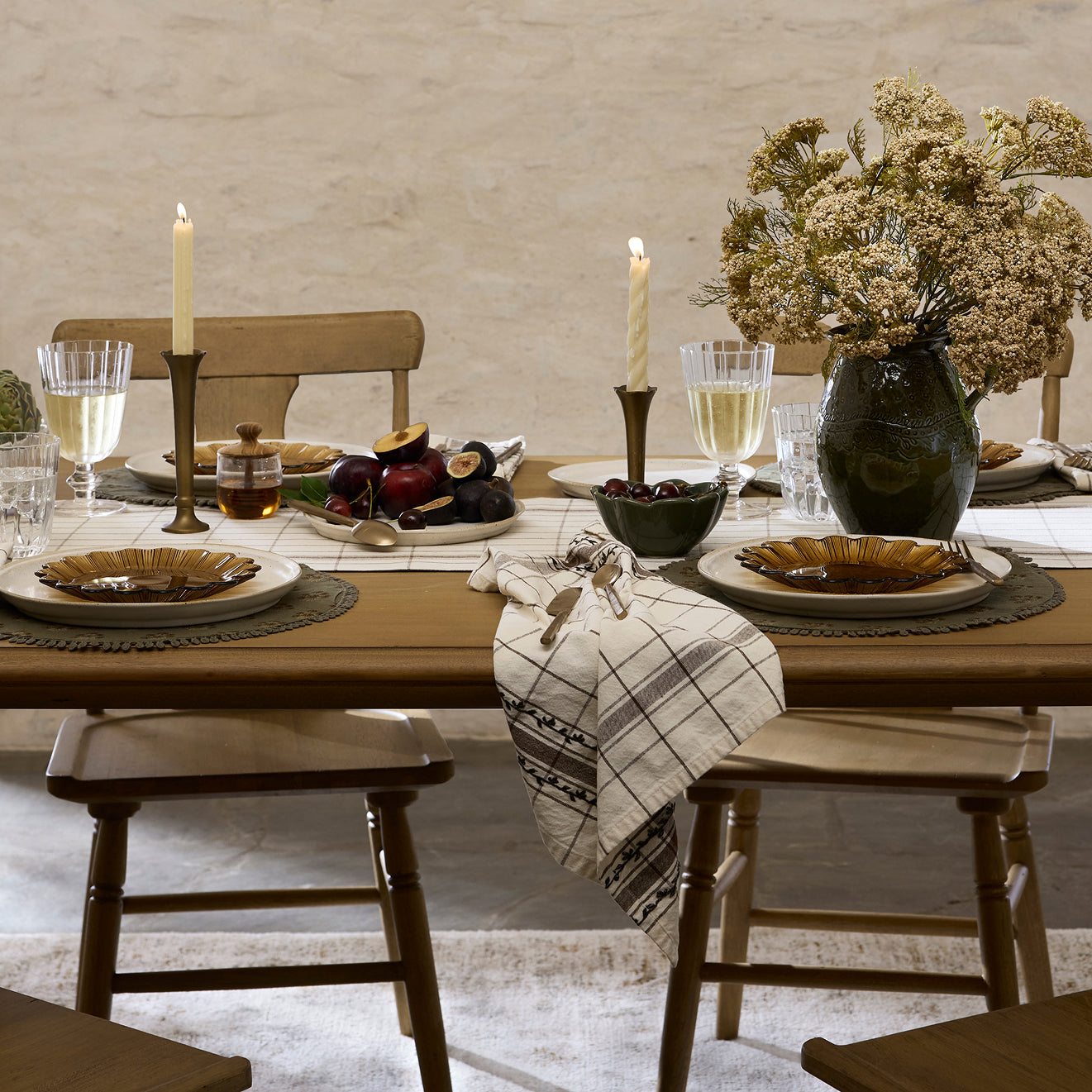 Dining table set with plates, glasses, candles, and a vase with flowers in a rustic setting.