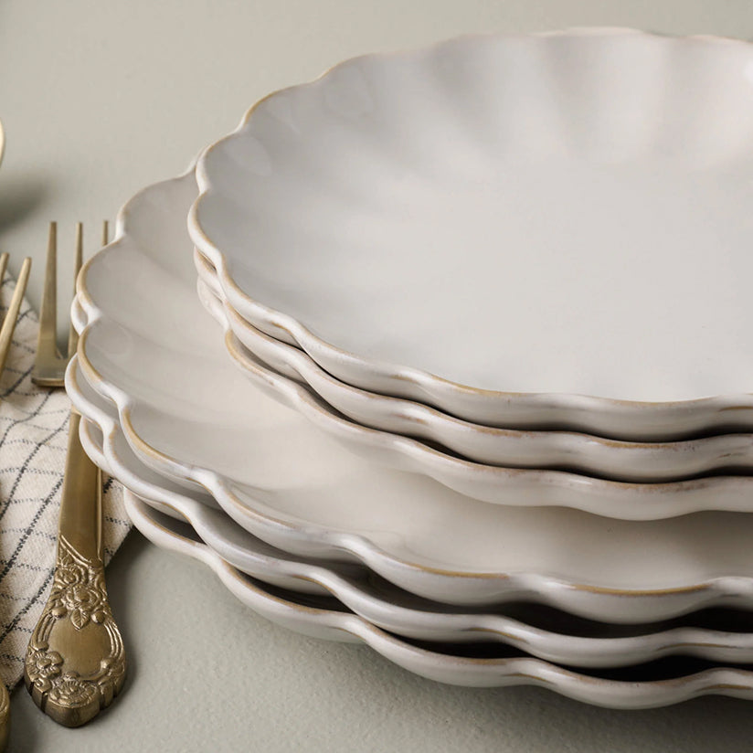 A stack of Magnolia's best-selling dinnerware, the scalloped collection on a light surface with a vintage brass fork.