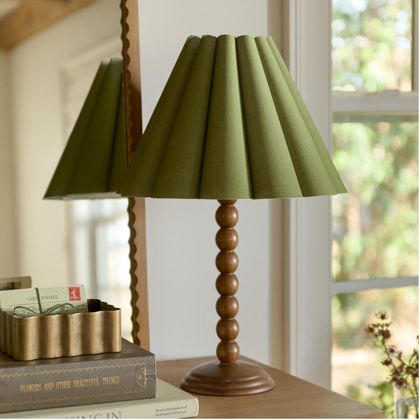 Table lamp with a green shade and wooden base on a surface near a window.