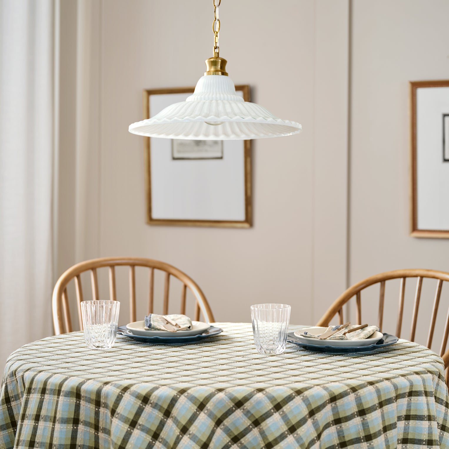 Dining table set with plates, glasses, and a plaid tablecloth in a room with framed pictures on the wall.