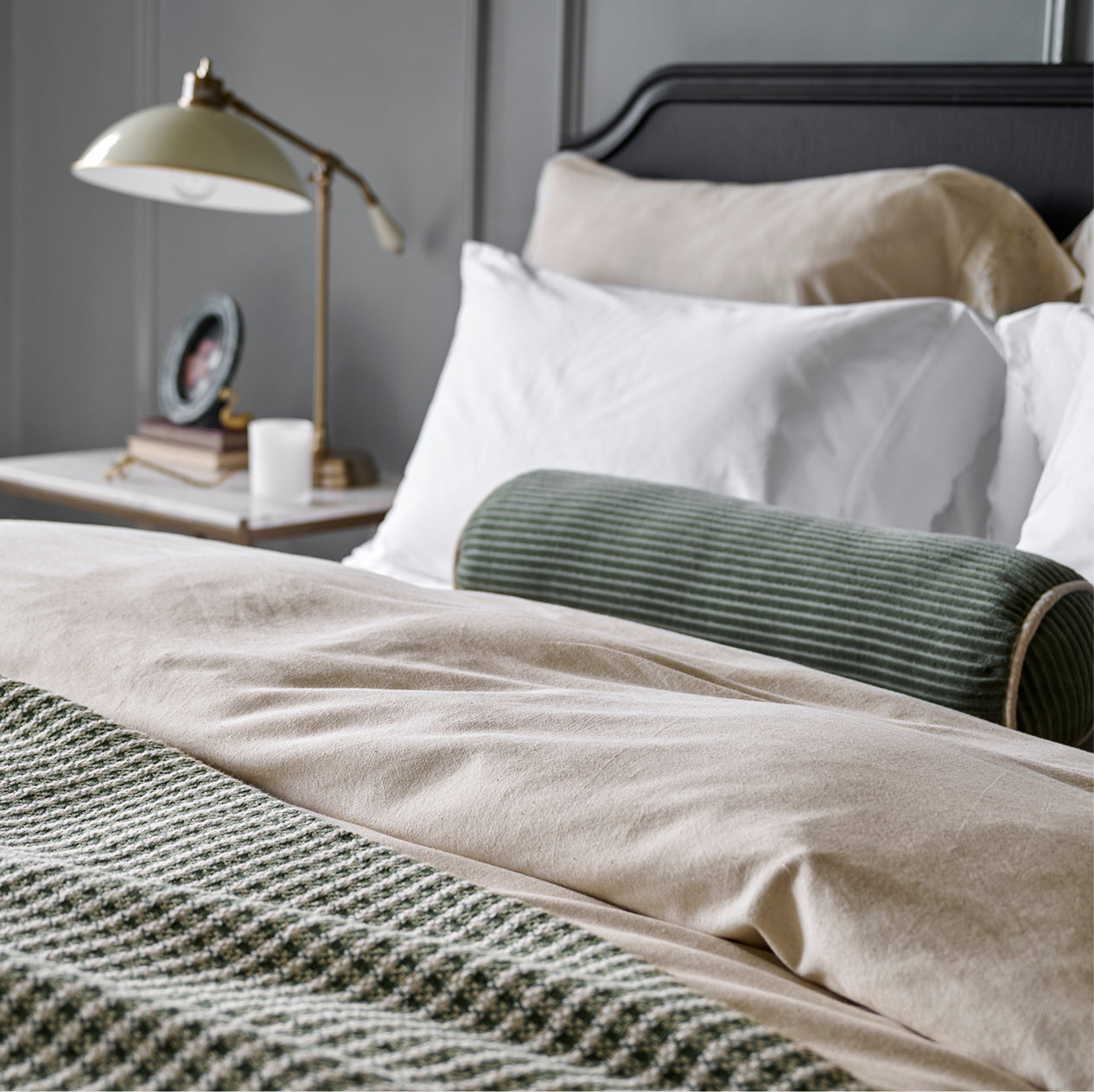 Neatly made bed with white pillows and a green decorative pillow, nightstand with lamp and decor items.