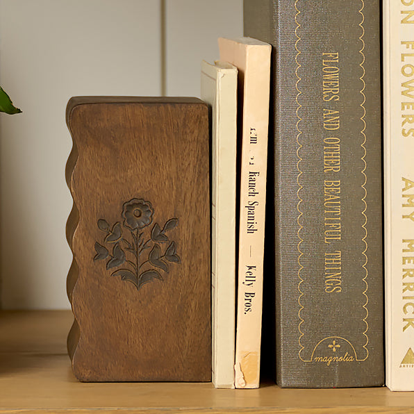 Wooden bookend with floral design next to books on a shelf