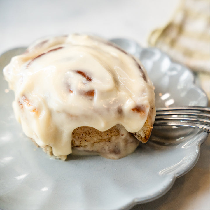 Cinnamon roll with white icing on a light blue plate with a fork.