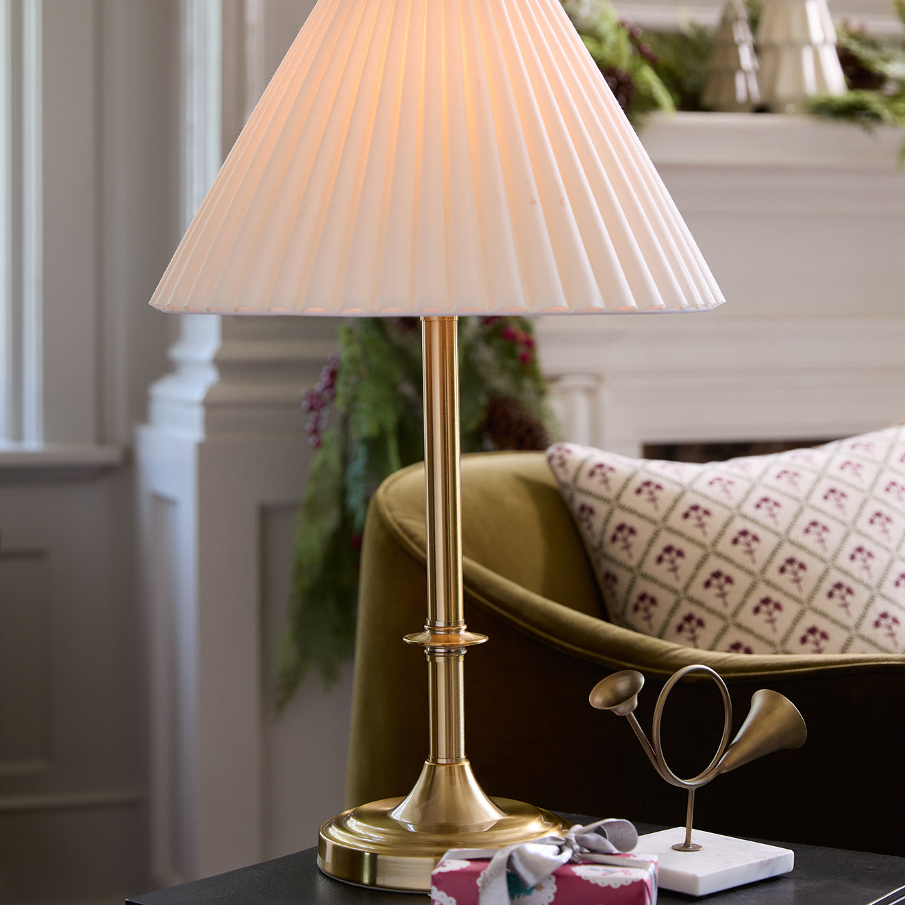 Gold table lamp with pleated white shade on a surface in a room setting.