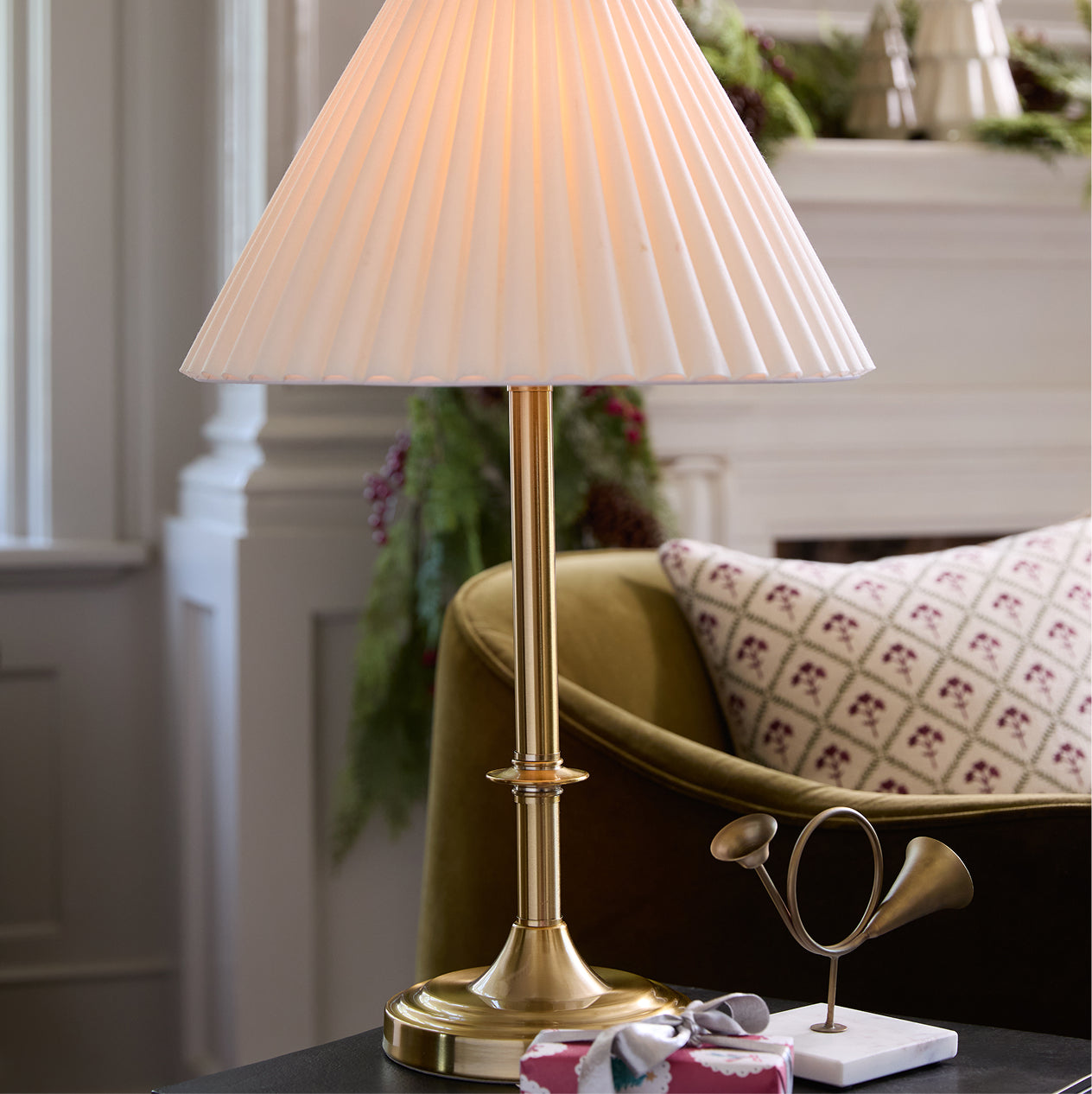 Gold table lamp with pleated white shade on a surface in a room setting.