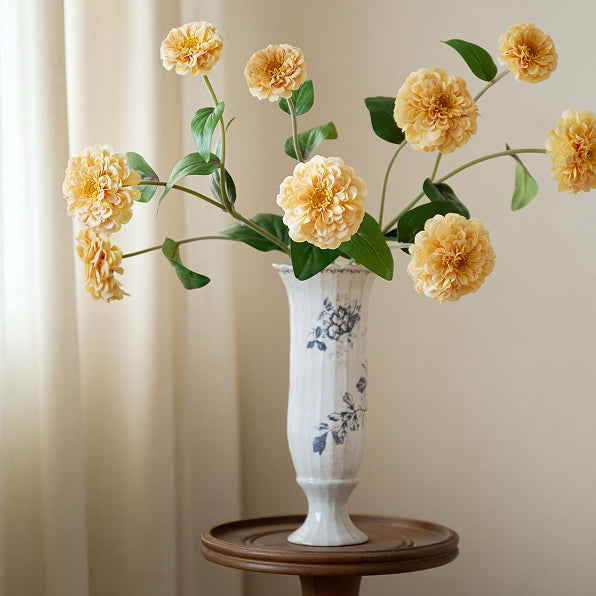 White vase with floral design on a wooden stand against a beige curtain background