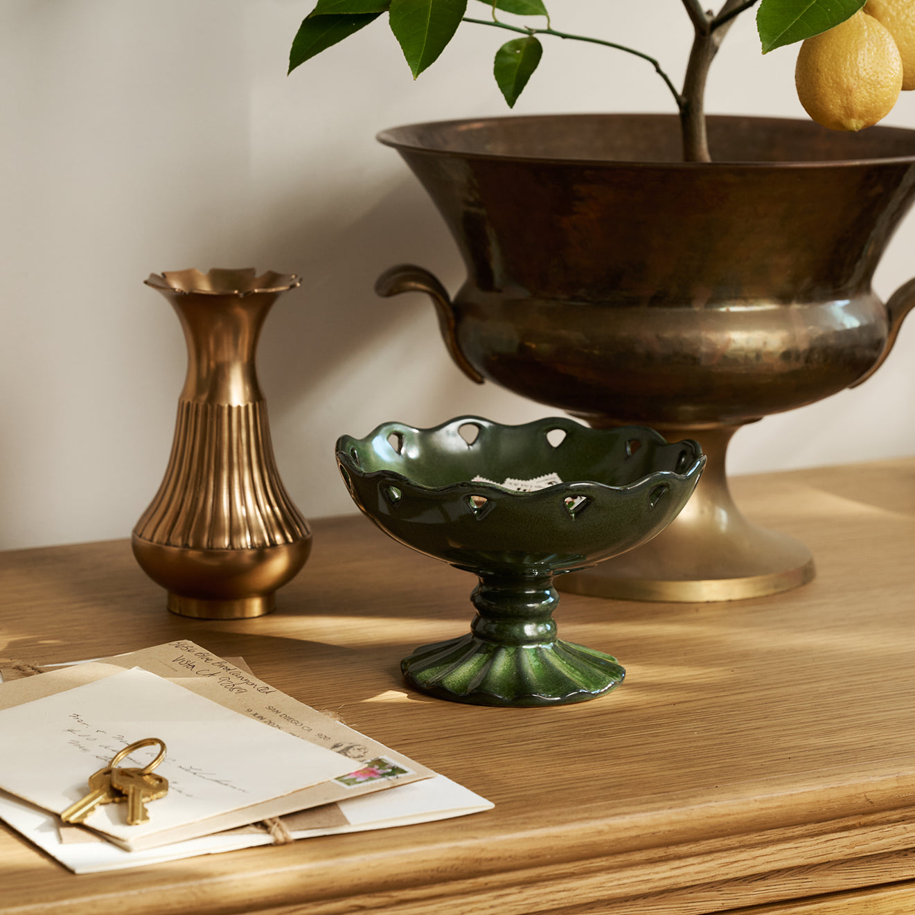 Decorative items including a brass vase, green ceramic bowl, and bronze urn on a wooden surface.