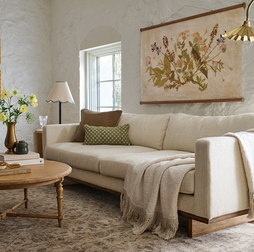 Cozy living room with a beige sofa, decorative pillows, and a floral painting on the wall.