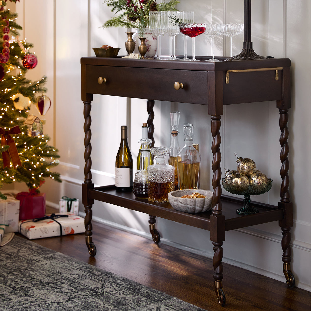 Wooden bar cart with drinks and decor in a festive room with a Christmas tree.