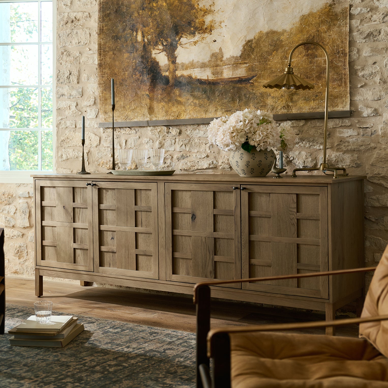 Wooden sideboard in a room with stone walls and a large painting above it.