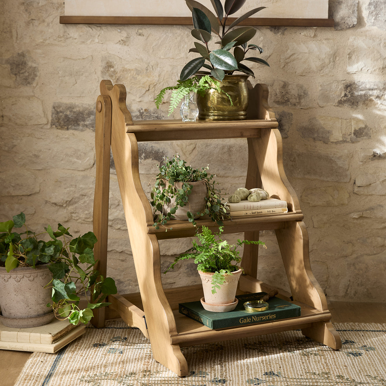 Wooden plant stand with potted plants against a stone wall.