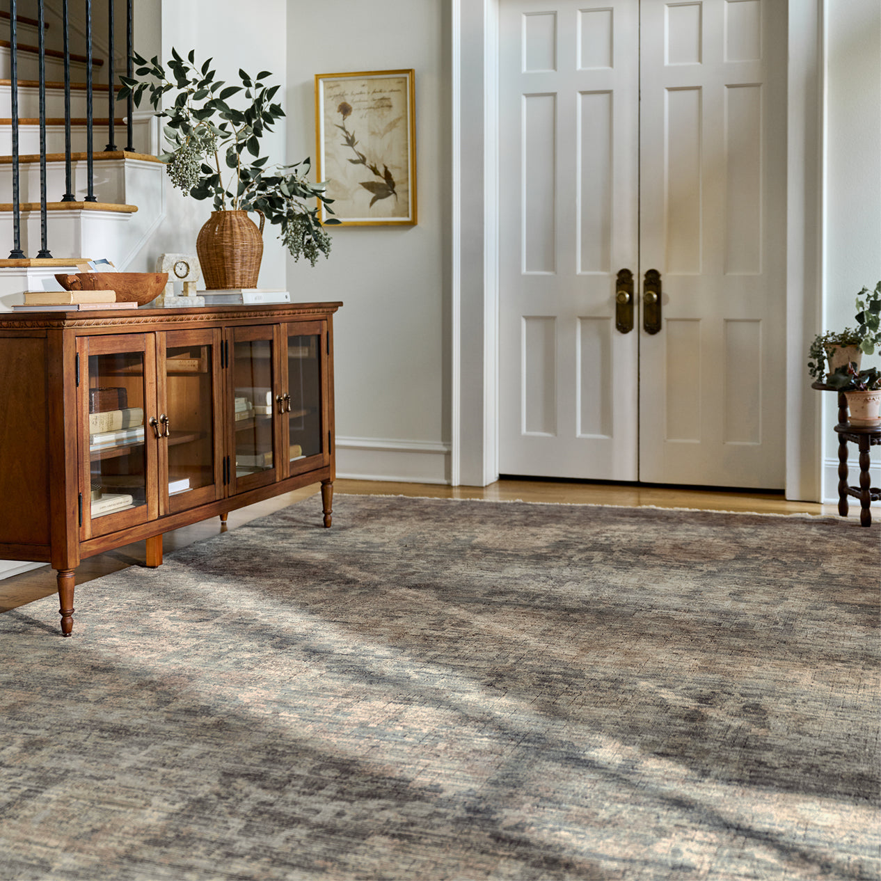 Wooden sideboard with glass doors in a room with a textured gray rug and white walls.