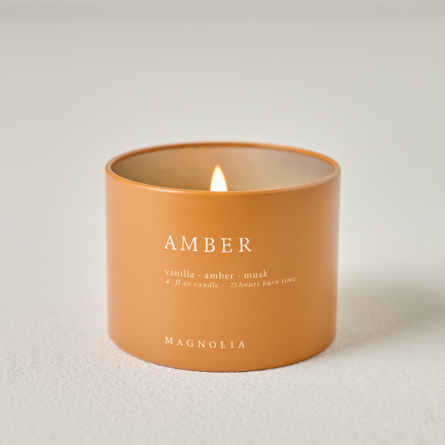 Magnolia Amber Candle Tin shown burning