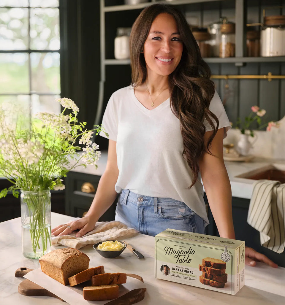 Joanna Gaines in her butler's pantry with a sliced loaf of Magnolia Table banana bread and a box of frozen Magnolia Table banana bread on a counter.
