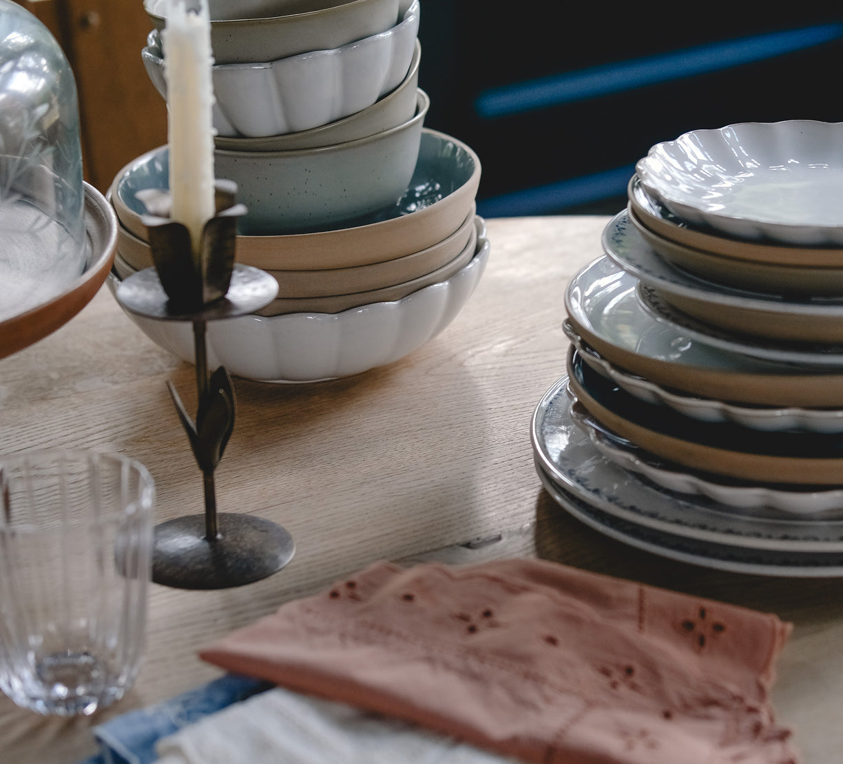 Stacked ceramic bowls on a wooden table with a candle and glasses.