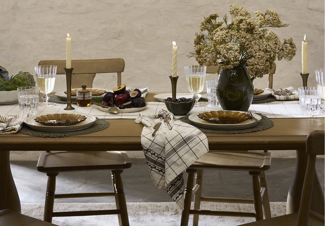 Dining table set with plates, candles, and flowers in a rustic setting.