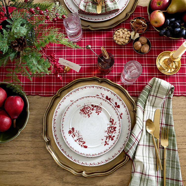 Decorative Christmas table setting with red plaid tablecloth, gold charger plate, and white plate with red floral pattern.