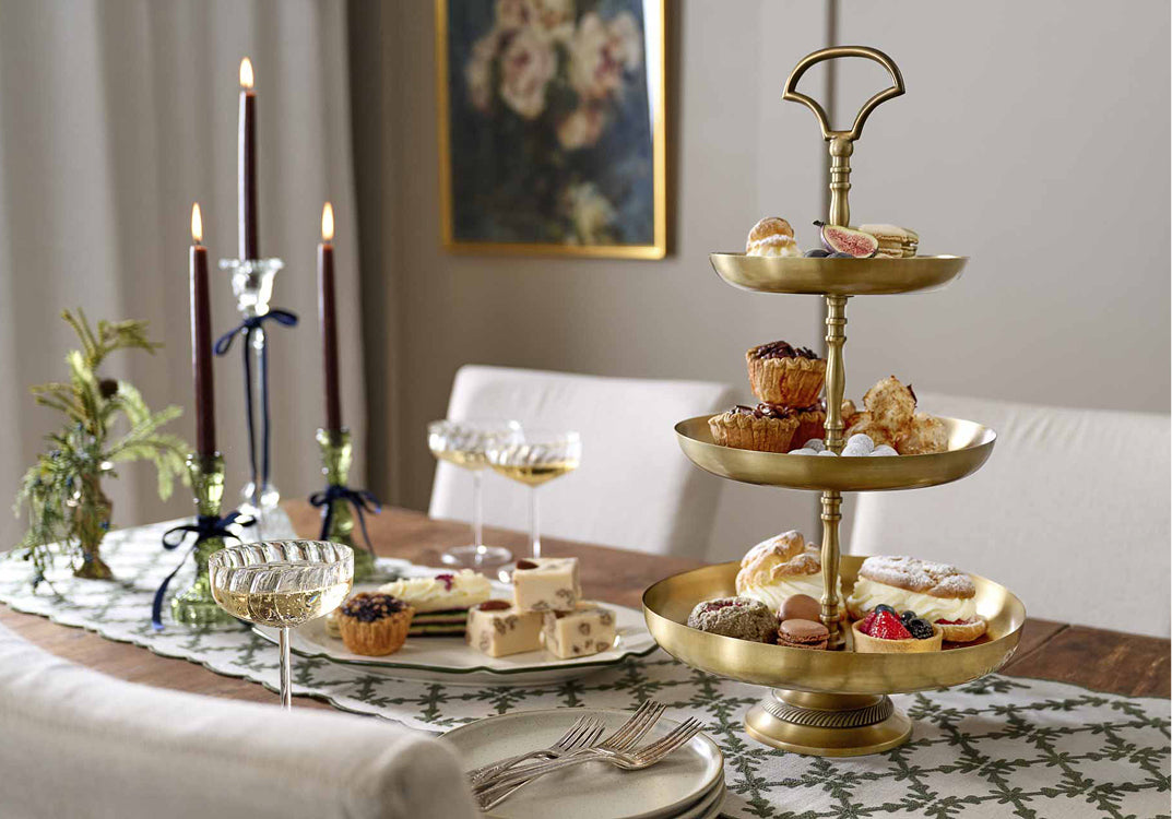 Holiday tabletop with three tier food server, lit candlesticks and a plate of cheese and desserts,