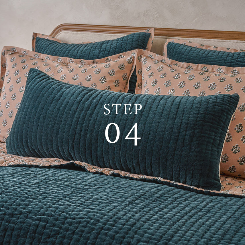 Teal textured pillow with 'STEP 04' text on a bed with floral-patterned pillows.  Shop pillows and throws.