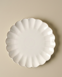 White ceramic plate with scalloped edge on a beige background