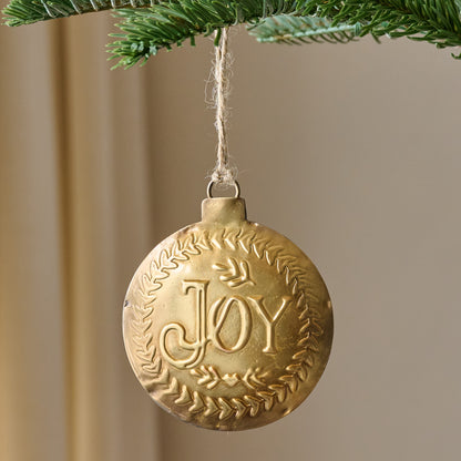 Pressed Metal Joy Ornament shown hung from tree