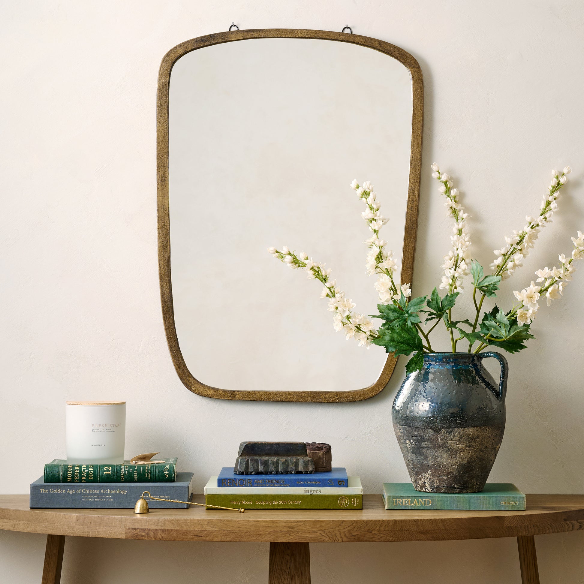 Jameson Aged Brass Framed Mirror on the wall above console tab with coffee tables, candle and floral vase