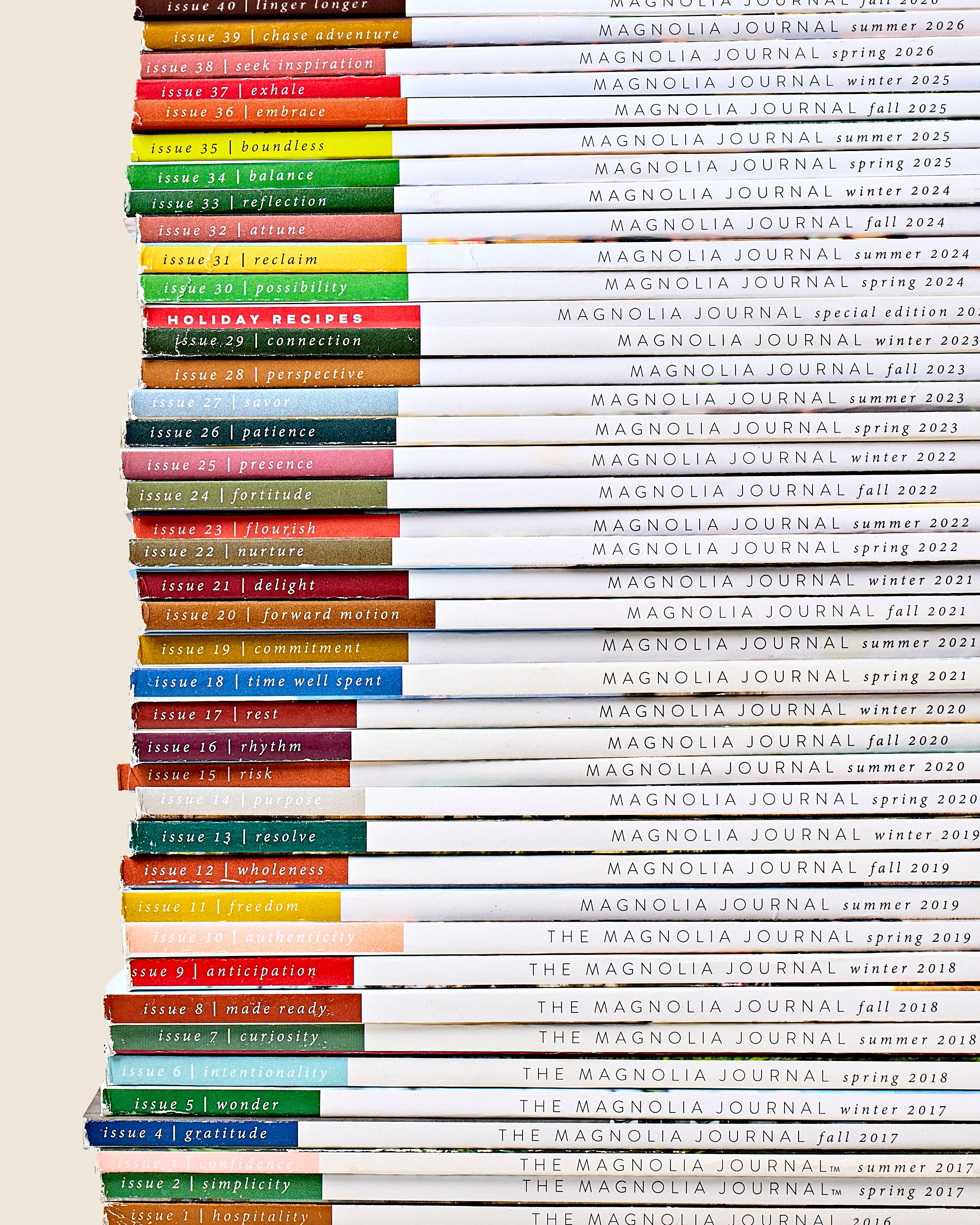 A close-up vertical stack of hardcover journals showing the spines and covers of multiple issues of The Magnolia Journal, with colorful title bands and white covers.