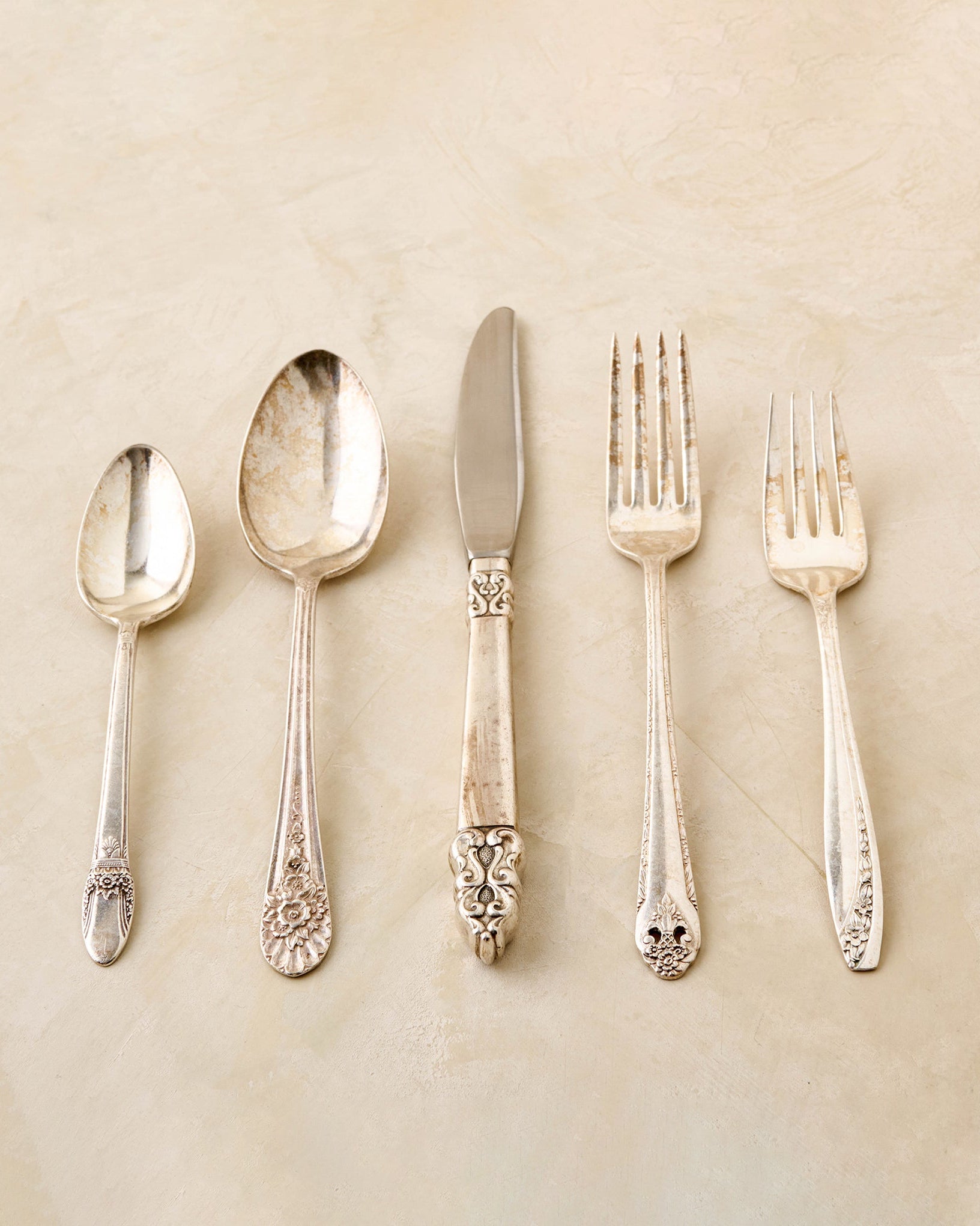 Set of silverware including spoons, a knife, and forks on a beige background