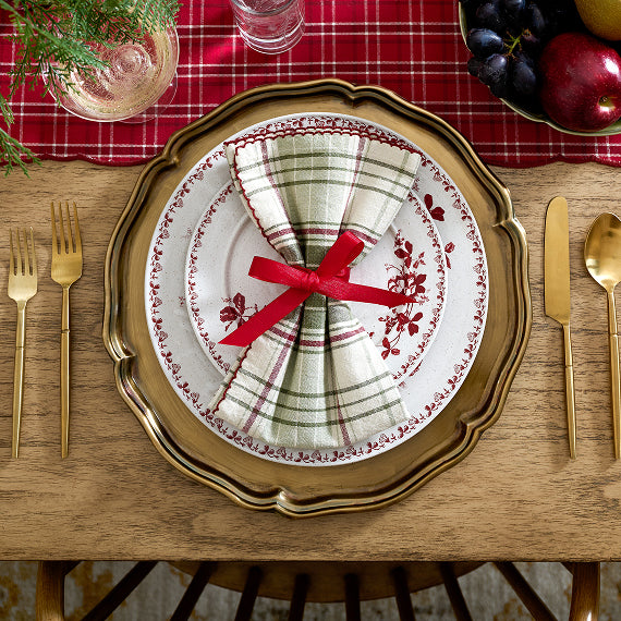 Dining table setting with a decorative plate, napkin, and cutlery on a red checkered tablecloth.