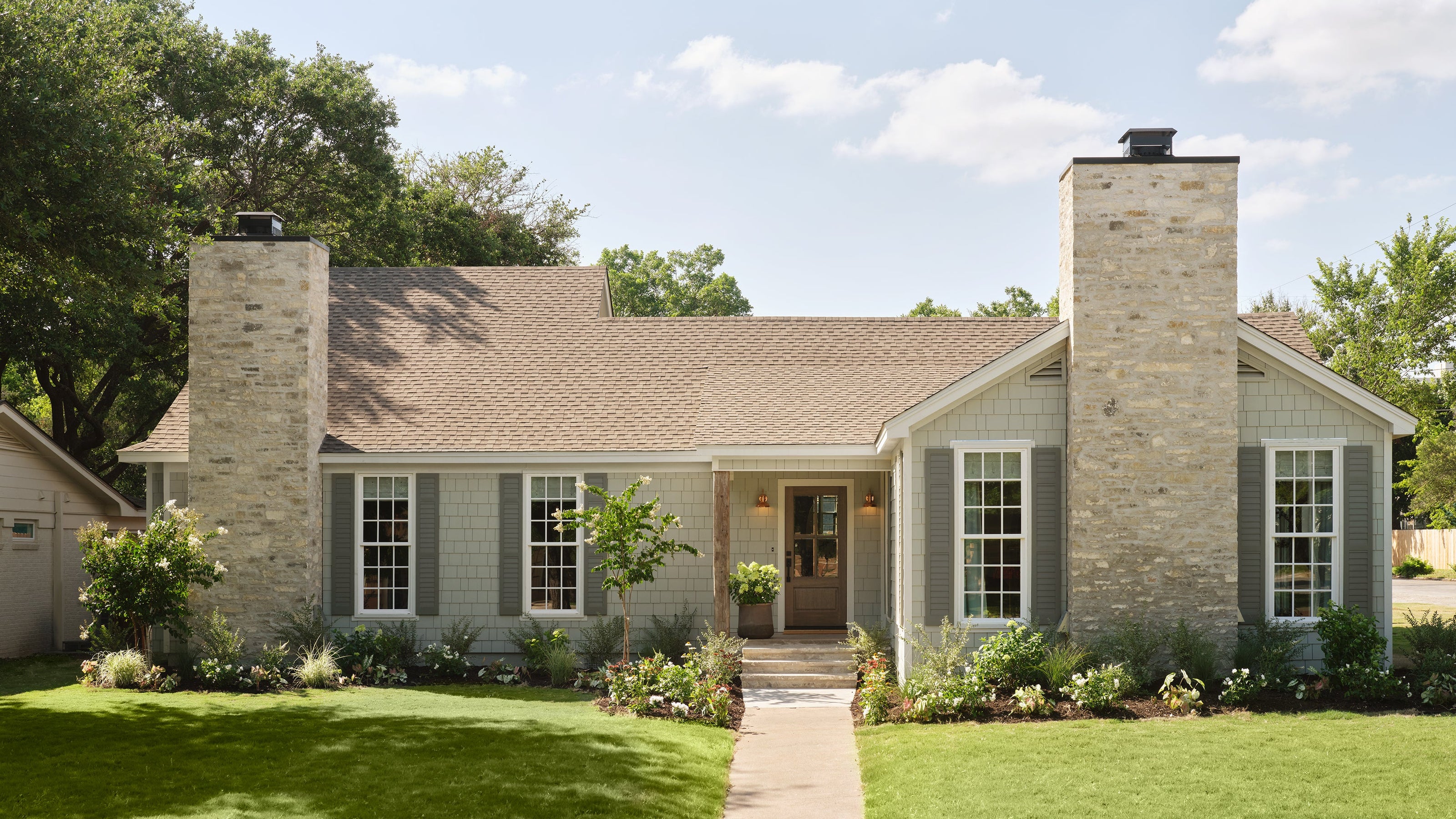 Stylish house with stone facade and green lawn under a clear blue sky