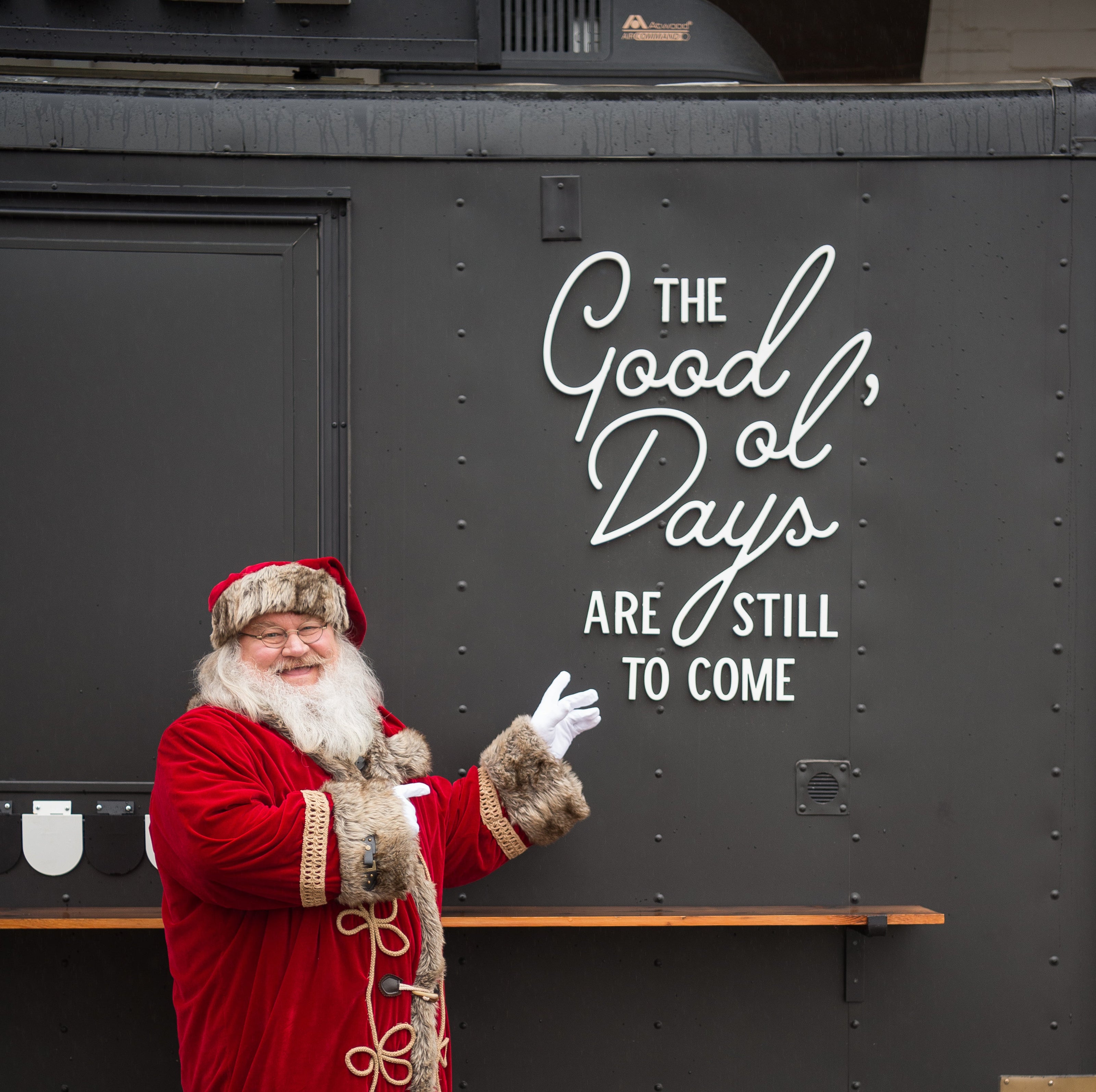 Person in a red Santa Claus outfit standing in front of a dark wall with text.